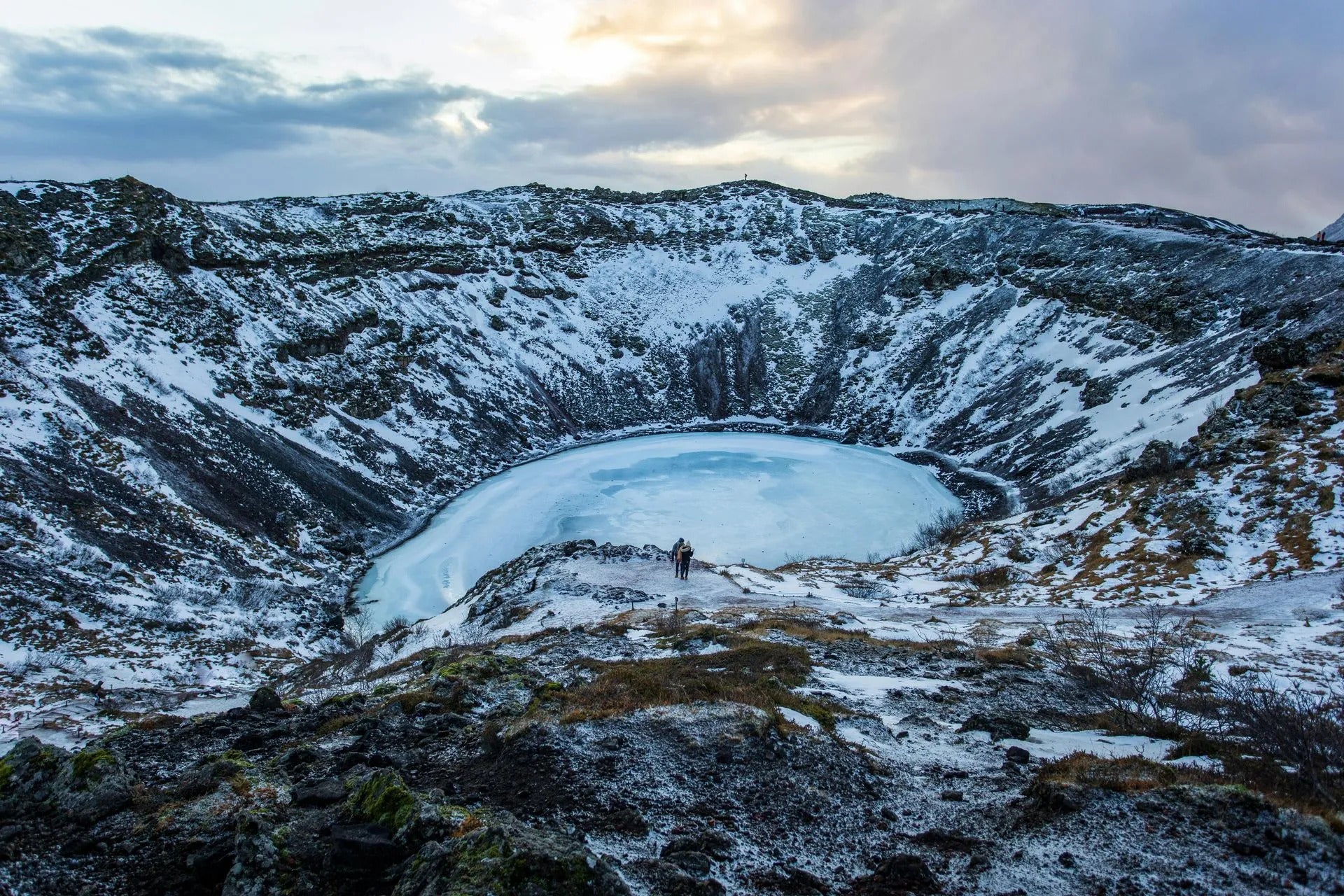 Kerid Crater frozen in winter with snowy cliffs surrounding the icy blue lake on a Golden Circle tour.