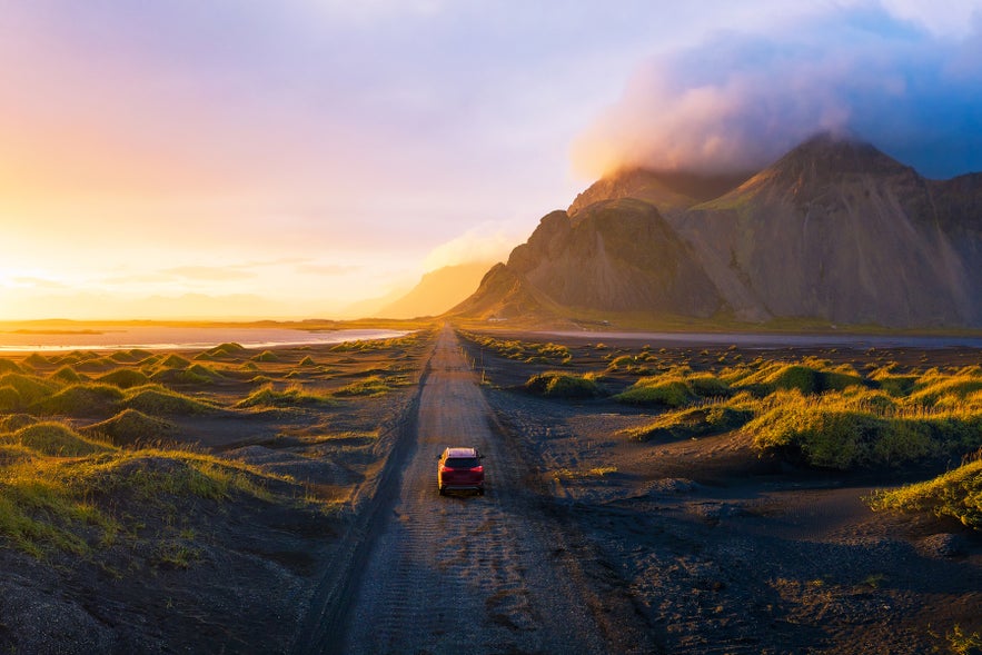 Car driving along a scenic Icelandic road in summer with green fields and distant mountains.