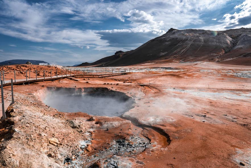 Steam rises from a bubbling mud pool as visitors follow a boardwalk at Hverir near Namaskard Pass in North Iceland.