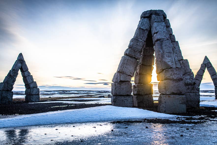 Sunlight shining through the stone arches of the Arctic Henge in Raufarhofn, North Iceland, with snow and ice in the foreground.