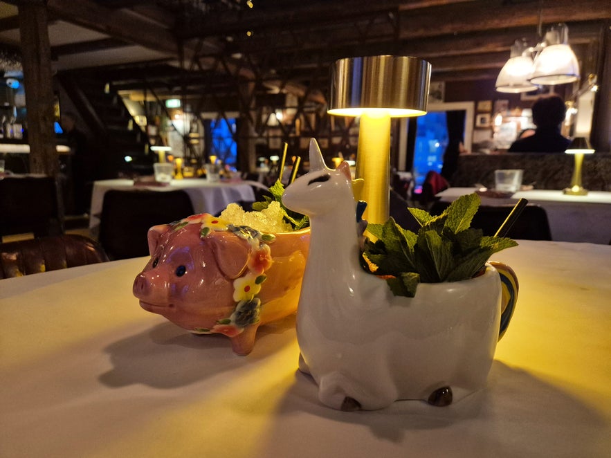 S&aelig;ta Sv&iacute;ni&eth; Reykjavik cocktails served in playful pig and unicorn cups, shown on a cozy table inside the warm, rustic gastropub.