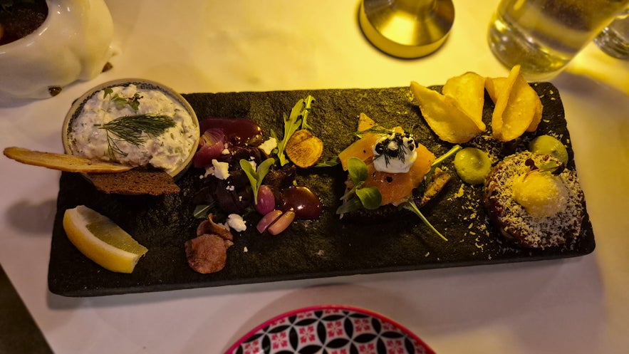 S&aelig;ta Sv&iacute;ni&eth; Icelandic tasting platter with horse tartar, puffin, flatkaka with arctic char, and cod dip served on a slate board in Reykjavik.