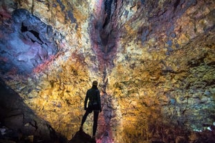 A man stands in the depths of Thrihnukagigur crater volcano with beautiful colors in the background.