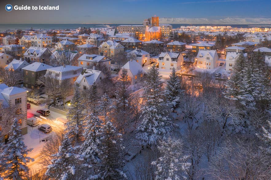 Vista aerea invernale su Reykjavik, Islanda, con case e alberi innevati illuminati da luci calde durante l’ora blu.