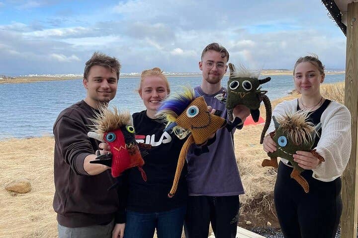 Four young people smiling together outdoors holding knitted toys by the water in Iceland.
