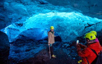 A woman poses for a photo in front of the shimmering walls of an ice cave in Iceland.