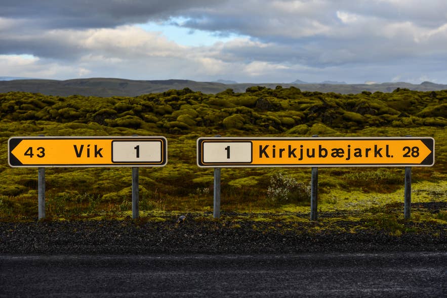 Road signs on Iceland’s Route One showing distances to Vik and Kirkjubaejarklaustur, surrounded by moss-covered lava fields in southern Iceland.