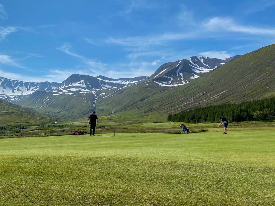 Siglufjörður Golf Club in North Iceland with players on green and snow-capped mountains backdrop. Siglufjörður Golf Club in North Iceland with players on green and snow-capped mountains backdrop.