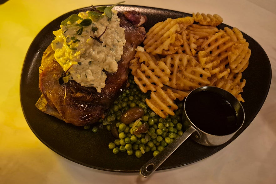 S&aelig;ta Sv&iacute;ni&eth; Icelandic lamb shoulder served with waffle fries, peas, sauce, and creamy topping, part of the hearty tasting menu in downtown Reykjavik.