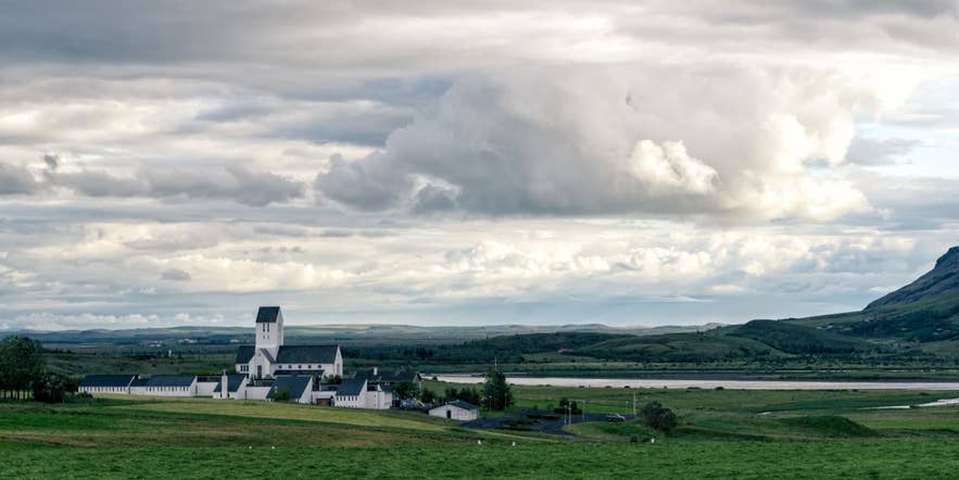 Die historische Kirche von Skalholt und die umliegende Landschaft unter dramatischem Himmel in Südisland.