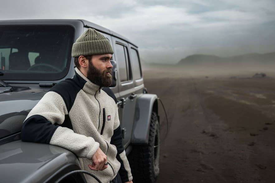 Reisender in 66°North-Kleidung neben einem Jeep in Islands rauer Natur
