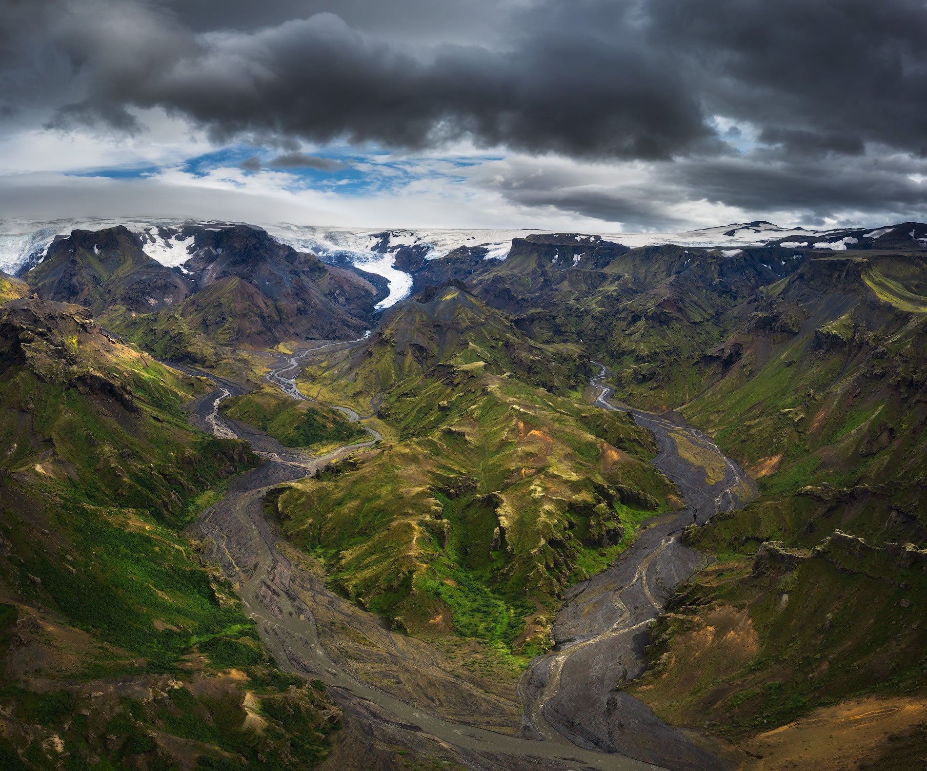 Thorsmork Valley in Iceland with braided rivers, green mountains, glaciers, and dramatic cloudy skies overhead.