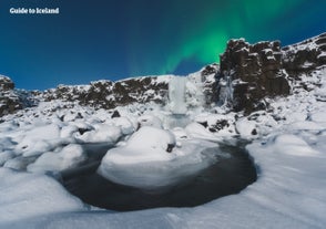 De Oxararfoss waterval in het Thingvellir National Park ziet er adembenemend uit omringd door een besneeuwd landschap met het noorderlicht boven je hoofd.