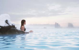 En dame som bader langs kanten av den dampende Earth Lagoon omgitt av damp og lavastein.