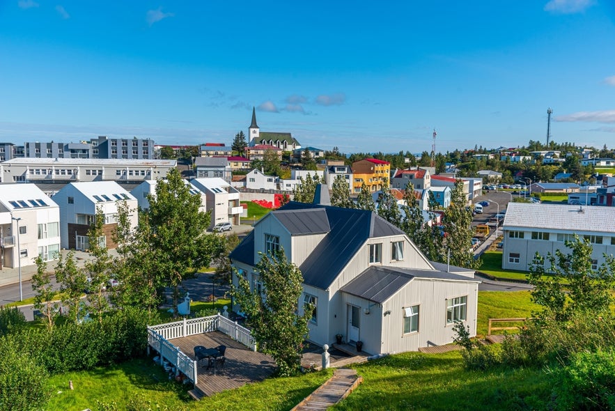 An aerial view of Borgarnes, Iceland with white house, greenery, colorful homes, and church steeple under clear blue sky.