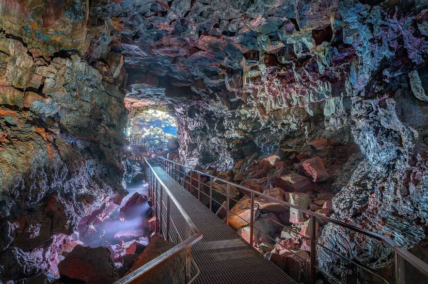 Walking path inside Raufarholshellir Lava Tunnel in Iceland in June, with colorful rock walls lit by soft lighting in the volcanic cave.