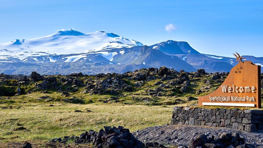 Entrance sign to Snæfellsjökull National Park in West Iceland with the snow-capped Snæfellsjökull glacier-volcano towering in the background on a clear day.