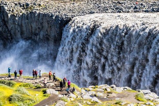 The powerfull falls of Dettifoss waterfall seen on a summer day with a small group of people standing near the edge.