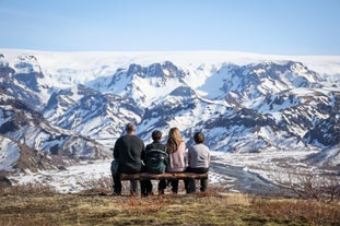 A family of four sits on a bench overlooking the snowy mountains of the Thorsmork Valley.