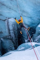 A person wearing a yellow jacket is seen ziplining over a glacier.