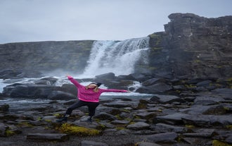A person poses for a photo with arms out in the air in front of a waterfall in Iceland.
