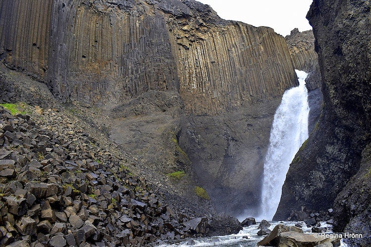 Litlanesfoss Waterfall flowing between towering hexagonal basalt columns and rugged rocky cliffs.