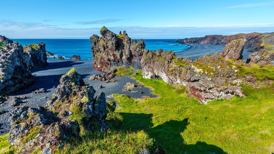 Djúpalónssandur black sand beach on the Snæfellsnes Peninsula, Iceland, with lava rock formations and blue North Atlantic Ocean under a clear sky.