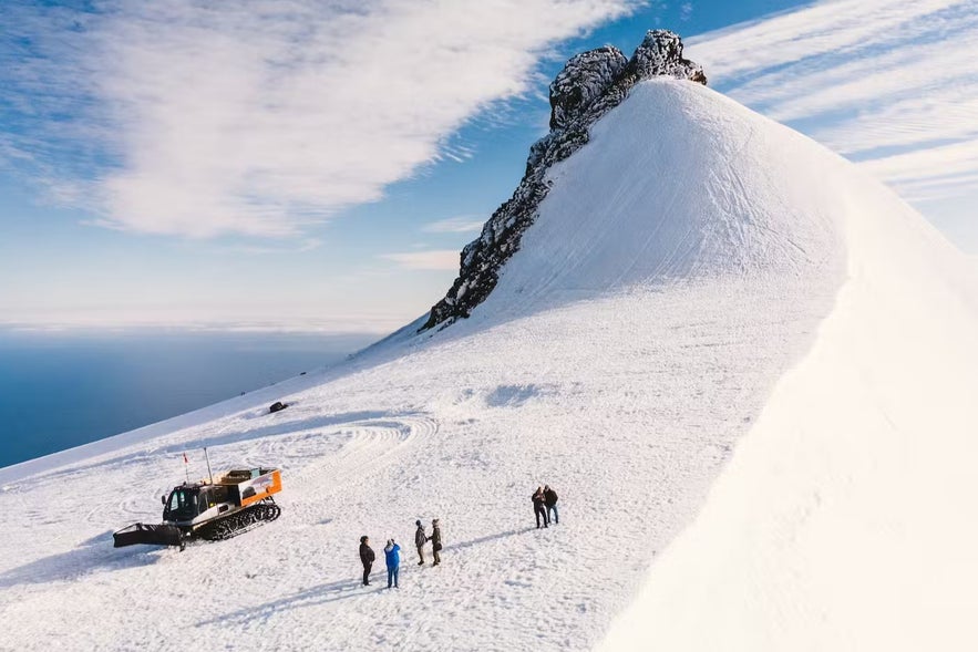 Snowcat tour with visitors exploring Snæfellsjökull glacier in West Iceland on a sunny day, with panoramic views of snow-covered peaks.
