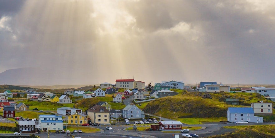 Colorful houses in Stykkishólmur under dramatic sun rays breaking through cloudy skies on Iceland’s Snæfellsnes Peninsula.