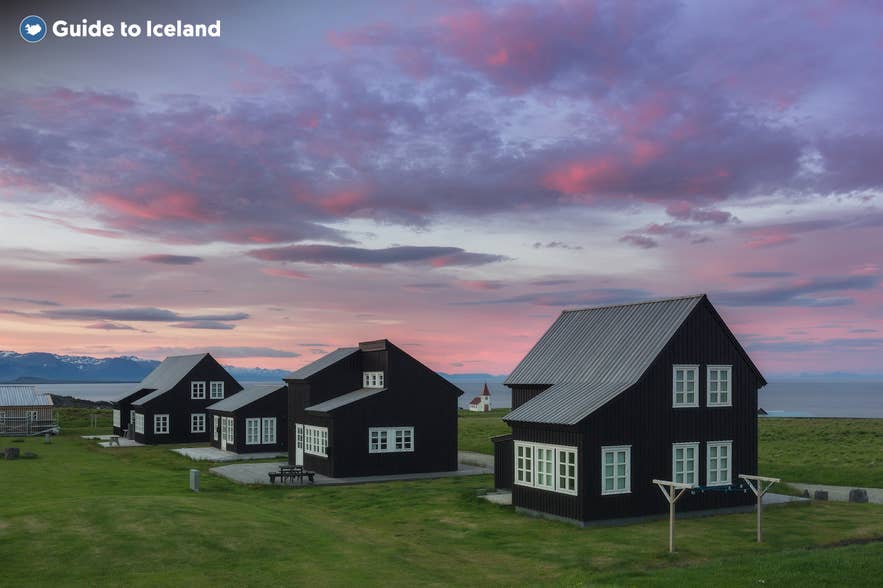 Black timber houses in the village of Hellnar on the Snæfellsnes Peninsula in Iceland, set against a colorful sunset sky.