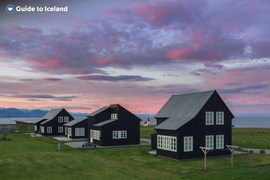 Black timber houses in the village of Hellnar on the Snæfellsnes Peninsula in Iceland, set against a colorful sunset sky.