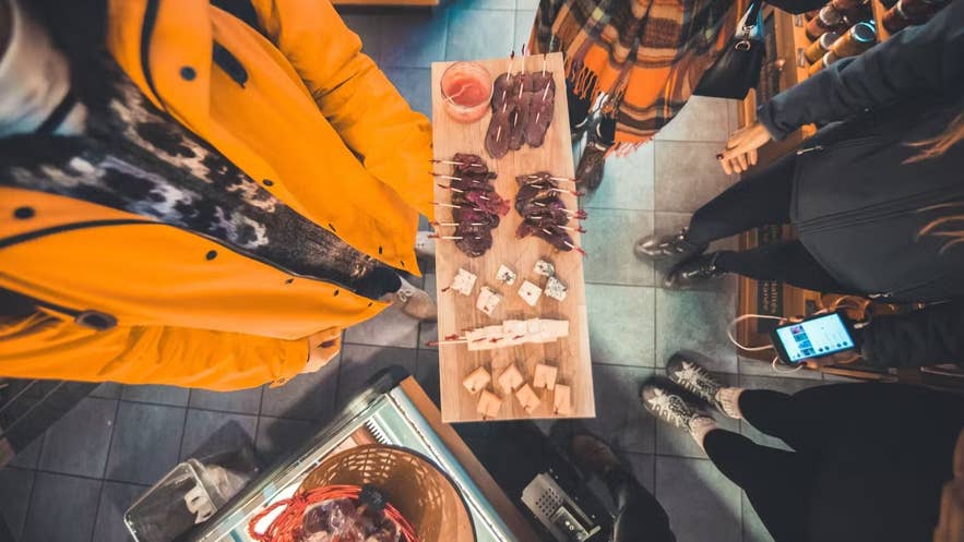 Tourists sampling traditional Icelandic delicacies, including hákarl (fermented shark) and cured meats, at a local food market.