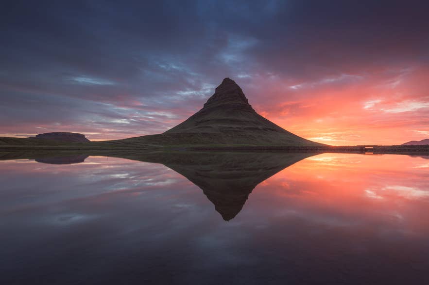 Kirkjufell mountain reflecting in still water at sunset on Iceland’s Snæfellsnes Peninsula, with dramatic skies highlighting its iconic peak.