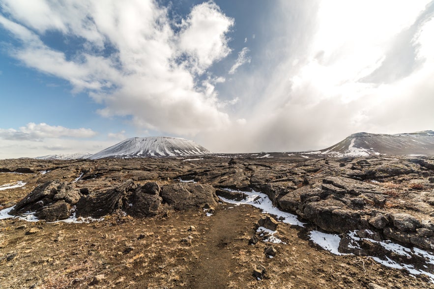 Hvannfell mountain rising above lava fields in North Iceland, with snow-dusted volcanic peaks and a rugged hiking trail.
