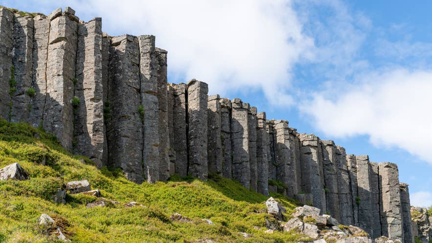 Tall basalt column cliffs of Gerduberg rising above green hills on the Snaefellsnes Peninsula in Iceland.