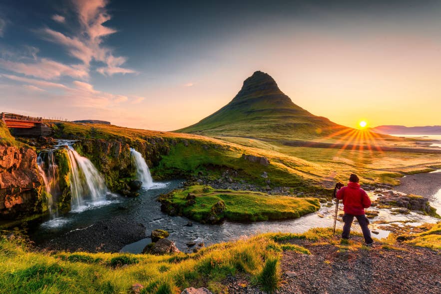 Hiker watching the sunset over Kirkjufell Mountain and Kirkjufellsfoss Waterfall on the Snaefellsnes Peninsula in Iceland.