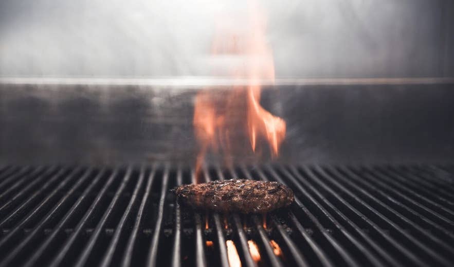 Beef burger patty grilling over open flames on a hot grill at Tommi&rsquo;s Burger Joint in Iceland.