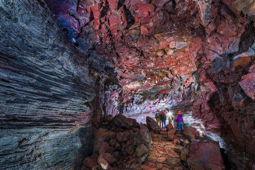 Visitors exploring the colorful red and grey volcanic walls of Raufarholshellir Lava Tunnel, a hidden gem along Iceland's South Coast