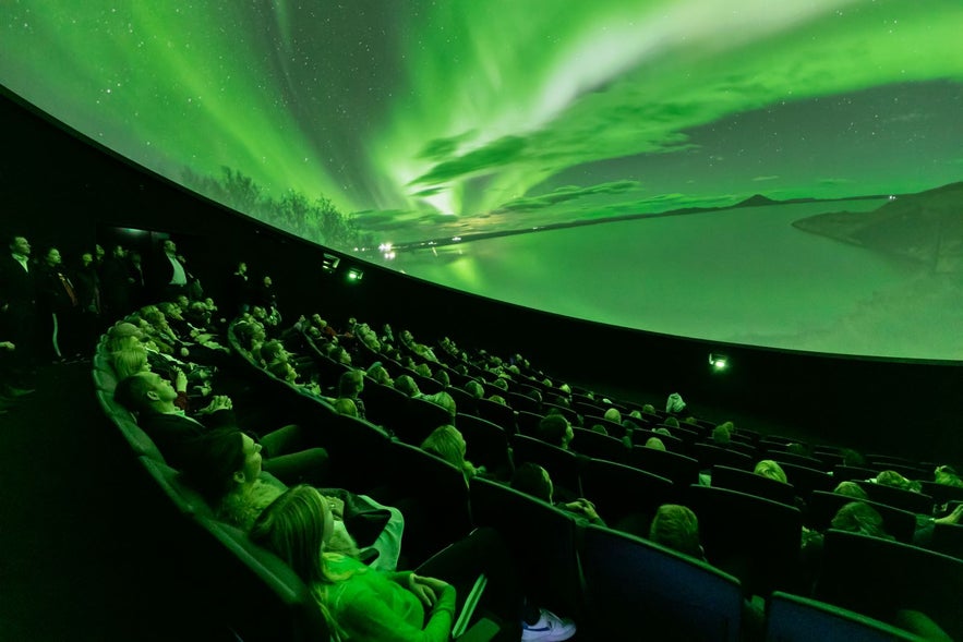 Visitors watching a northern lights show at Perlan planetarium in Reykjavik, Iceland, with immersive dome projections.