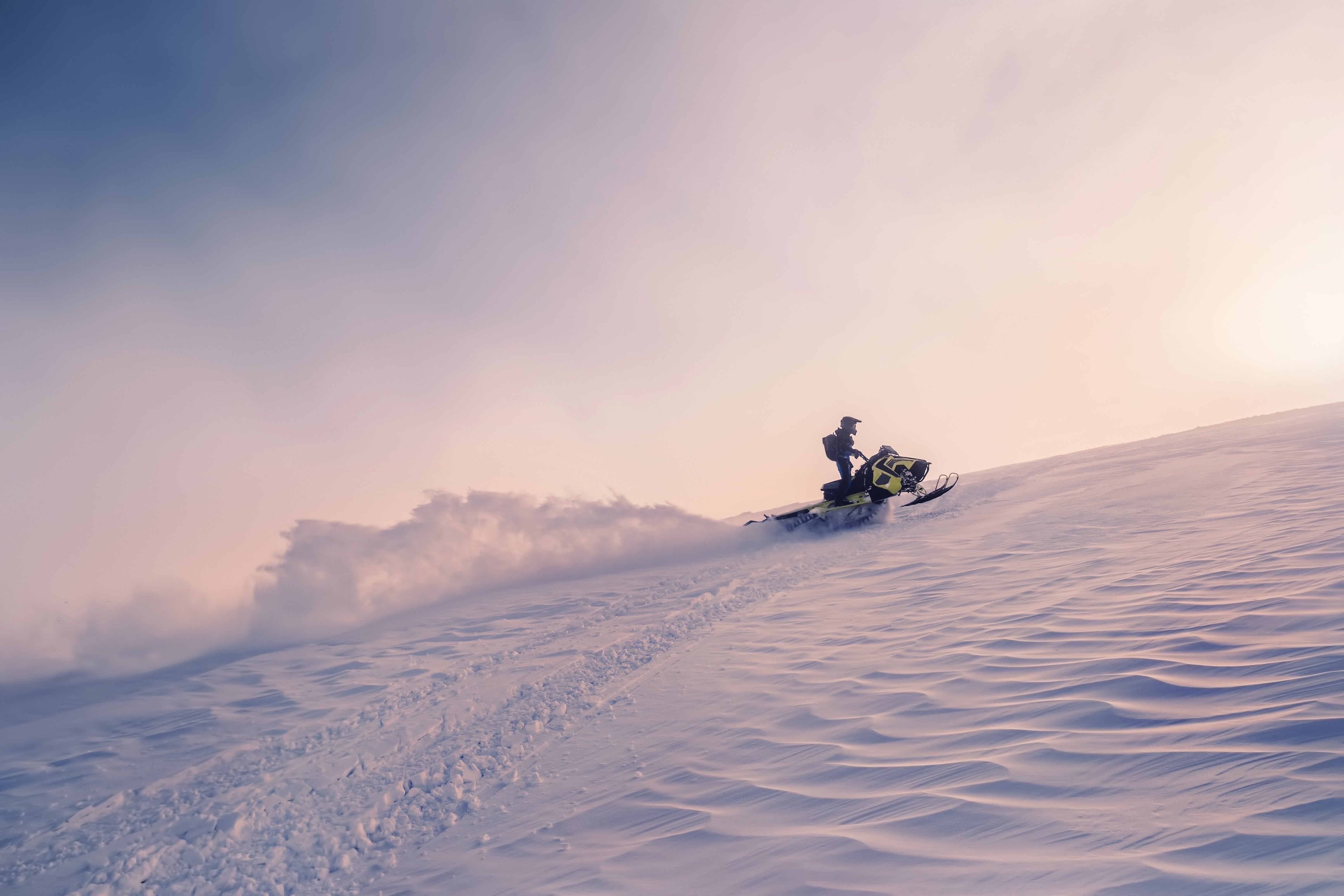 A rider carves through snow at sunset during a snowmobile tour on Langjokull Glacier.