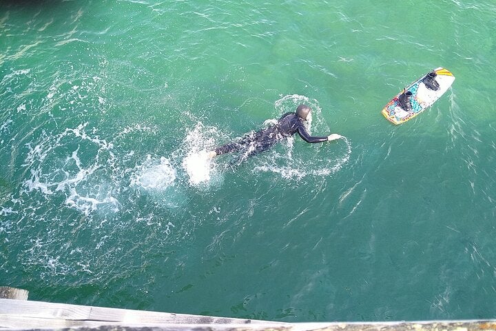 An overhead view of a person swimming to their wakeboard at Holt Beach in the Westfjords.