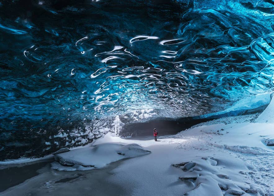 Podróżny zwiedzający niebieską jaskinię lodową w parku narodowym Vatnajokull w pobliżu laguny lodowcowej Jokulsarlon podczas wycieczki z przewodnikiem po południowym wybrzeżu Islandii.