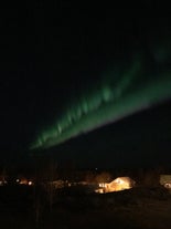 The northern lights shine in the sky above the Icelandic countryside.