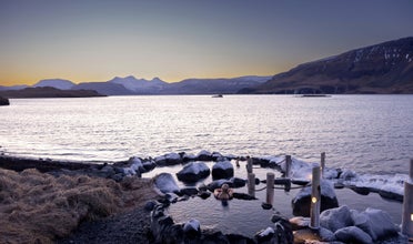 A person relaxes in a natural hot spring and enjoys the view of the Hvalfjordur fjord and the nearby mountains.