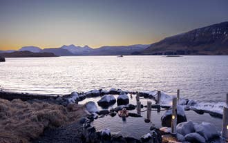 En person slapper af i en naturlig varm kilde og nyder udsigten over Hvalfjördur-fjorden og de nærliggende bjerge.