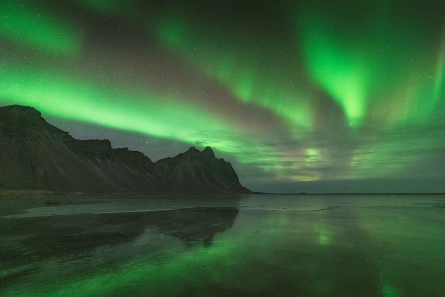 北极光映照韦斯特拉霍恩山（Vestrahorn Mountain），并倒映在冰岛南部斯托克斯内斯（Stokksnes）的湿沙上。