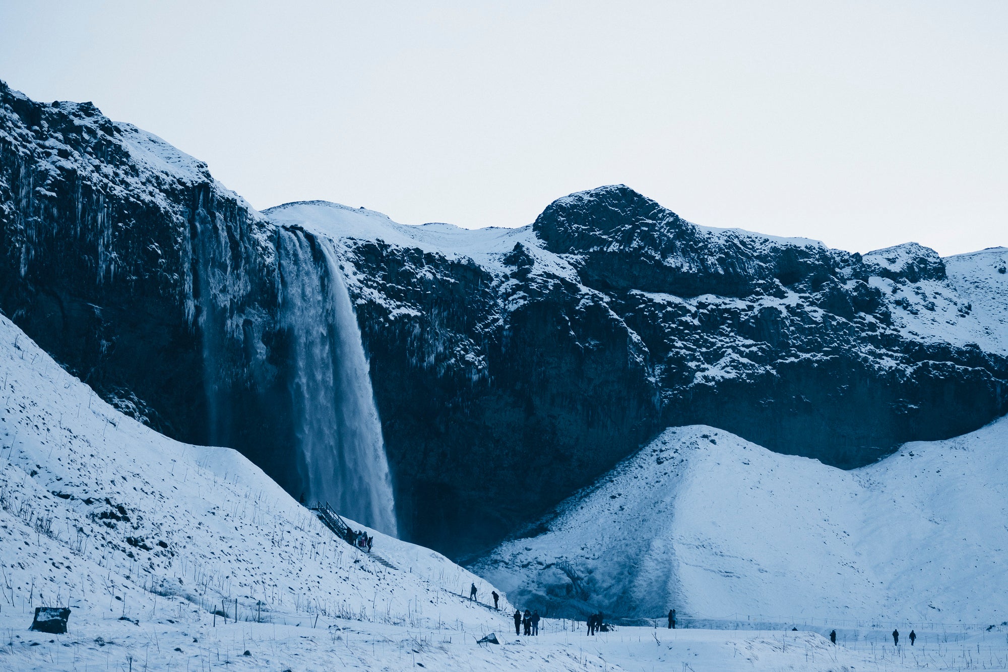 La cascade apparemment figée de la chute d’eau de Seljalandsfoss tombe sur un champ glacé où des touristes se tiennent lors d’un circuit sur la route circulaire.