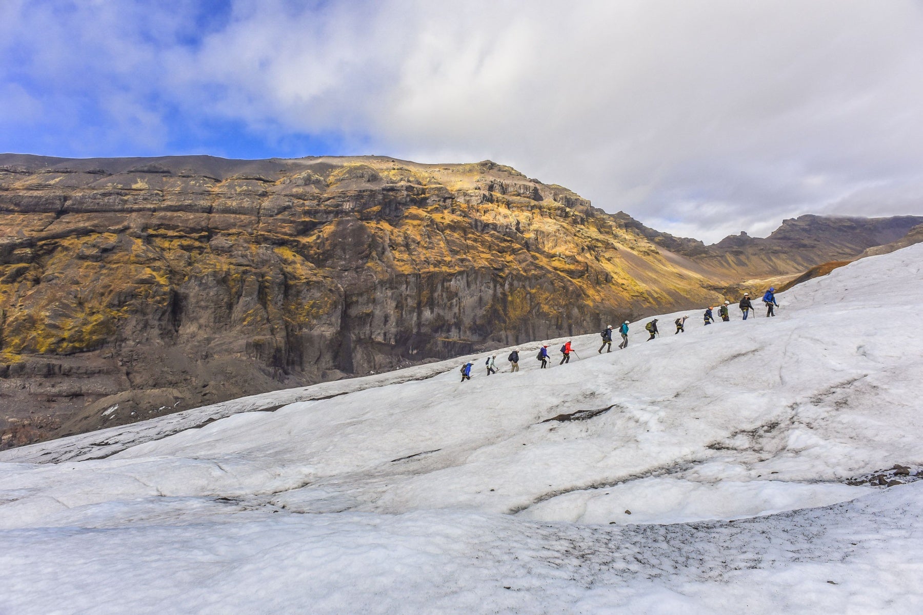 Group of hikers walking in a line across a glacier during a guided glacier hiking tour in Iceland.