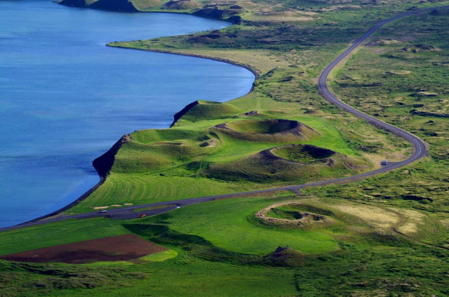 Aerial view of a coastal road in Iceland winding past grassy volcanic craters beside the sea. Aerial view of a coastal road in Iceland winding past grassy volcanic craters beside the sea.