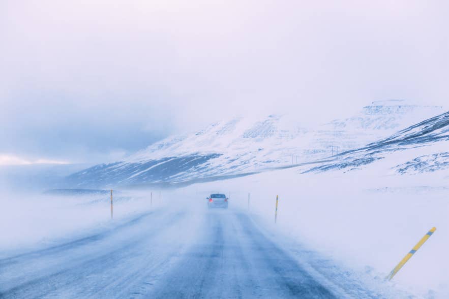 Car driving along a snow-covered road in Iceland during winter, with blowing snow and low visibility. Car driving along a snow-covered road in Iceland during winter, with blowing snow and low visibility.